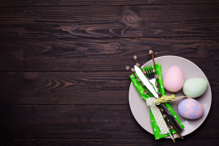 Easter table place setting with plate, cutlery and decor egg on dark wooden background, top view....