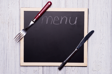 menu blackboard with knife and fork on rustik white wooden background with copy spaceの写真素材