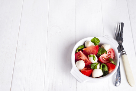 Italian traditional caprese salad . Mozzarella cheese, tomatoes and basil herb leaves on bowl and wine bottle over wooden table. Top viewの写真素材