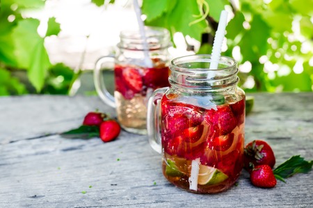 Fresh red strawberry lemonade in mason jar on a wooden table Against the background of grapevines. Summer drinks and cocktailsの写真素材