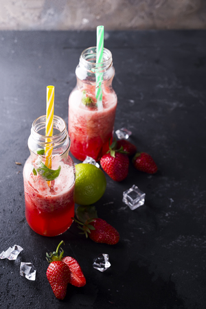 Strawberry smoothies in bottles with basil and lemon on a dark stone backgroundの写真素材