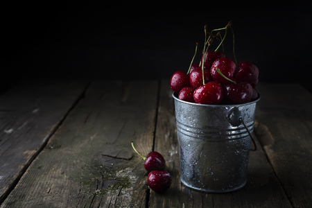 Fresh cherry In a bucket on dark old wooden background. copy spaceの写真素材