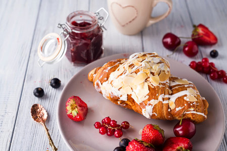 Croissants, cup, jam and berries on light gray background. Copy space. Healthy breakfast concept.