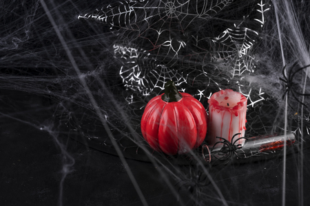Pumpkin, candle and a long glass with a red cocktail on the background of cobwebs and hats on a black background copy spaceの写真素材
