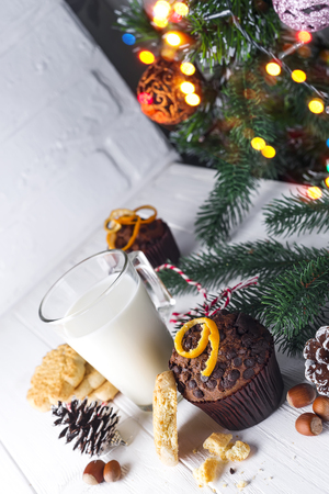 Cookie with milk, muffin, cookies and christmas tree on the table for Santa Claus, by Christmas decorations on Christmas lights bokeh backgroundの写真素材