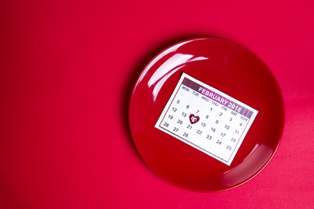 red plate with a piece of calendar on red background, flat lay copy spaceの写真素材