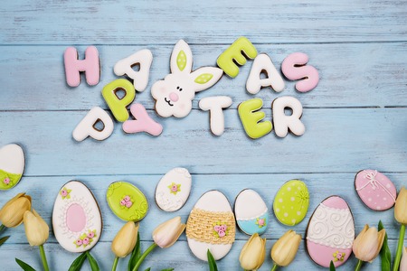 Easter cookies letter Happy Easter and colorful eggs with tulips on wood backgroundの写真素材