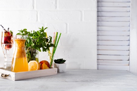 Orange lemonade in the decanter on a wooden tray with ftuits and mintの写真素材