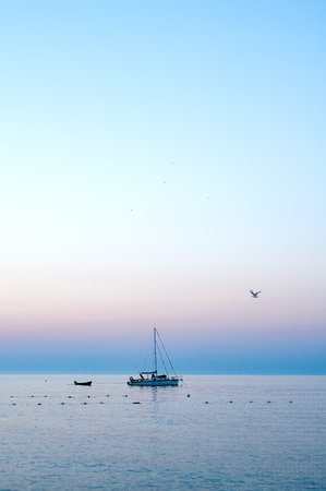 Boat on the sea smooth surface on a beautiful sunrise and flying seagulls on the sky backgroundの写真素材