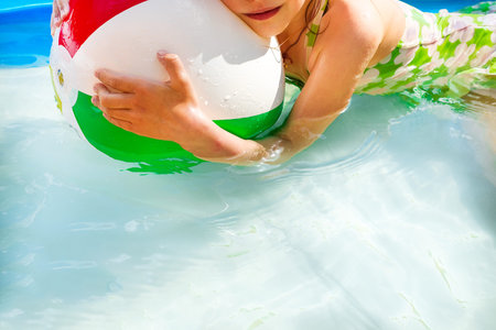 Little girl playing in outdoor swimming pool jumping into water on summer vacation in the courtyard...