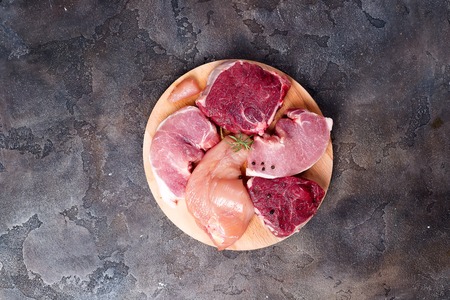 Mockup of raw chicken, beef and pork on cutting board set on wooden round board. Lean proteins.の写真素材