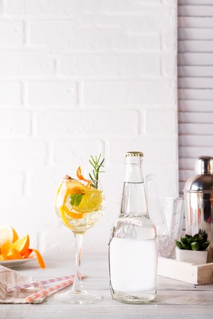alcohol cocktail with fresh fruits and berries with a bottle of tonic and a place under the text on the bottle on white wooden backgroundの写真素材
