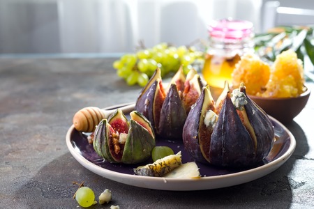 Gourmet appetizer of baked figs with goat cheese,walnuts and honey on ceramic plate and brown concrete background,の写真素材
