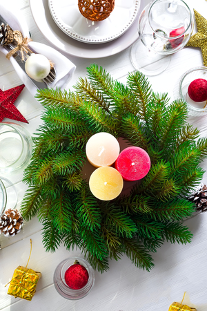 Christmas wreath with colorful big candles on a table with a Christmas table setting on a white wooden table , top view copy spaceの写真素材