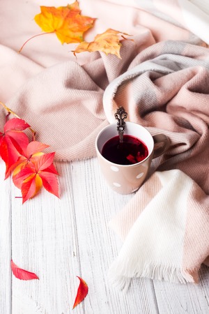 Autumn concept. A cup of healthy tea in yellow red leaves with beige scarf on white wooden background.の写真素材