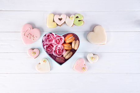 Hearts cookies and macaroons in box. Festive round blue box with cookies and Rose on white wooden background, flat lay with copy spaceの写真素材
