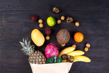 Paper bag of different healthy tropical fruits on dark woodenの写真素材