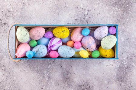 Easter colorful eggs painted in bright colors with straw nest in wooden box on stone
