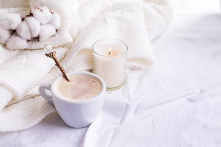 Bedding with a fluffy knitted plaid and cup of coffee, cotton flowers and candle. Cozy day. Flat lay, top viewの写真素材