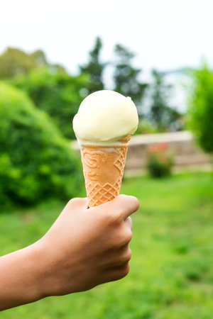 A young child hand holding a green ice cream cone on a nature