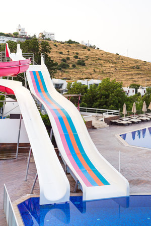 Slider in swimming pool with blue water and green trees