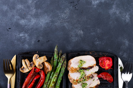 Grilled chicken breast on a cast iron skillet with grill vegetables on a stone background, flat layの写真素材
