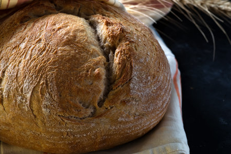 Round freshly baked rustic rye round bread with wheat ears and napkin close-up