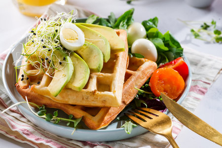 Belgian Waffles with avocado, eggs, micro green and tomatoes with orange juice on marble table.