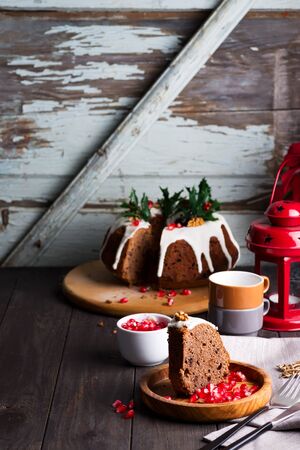 Christmas sliced chocolate cake with white icing and pomegranate kernels, cups and red lantern against the background of old wooden doorsの写真素材