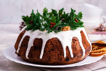 Christmas homebaked dark chocolate bundt cake decorated with white icing and holly berry branches close-upの写真素材