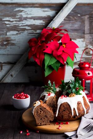 Christmas sliced chocolate cake with white icing and pomegranate kernels on a wooden dark background with red lantern and poinsettiaの写真素材