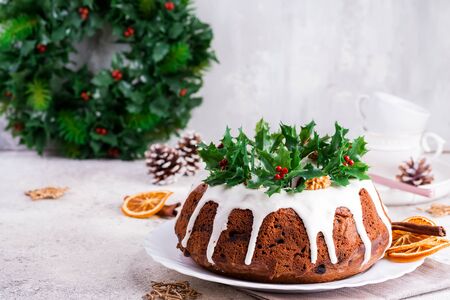 Christmas homebaked dark chocolate bundt cake decorated with white icing and holly berry branches on a light concrete backgroundの写真素材