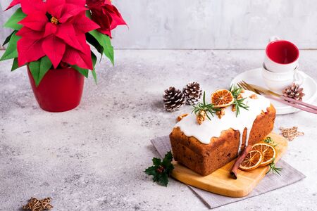Fruit loaf cake dusted with icing, nuts and dry orange on stone background. Christmas and Winter Holidays Poinsettia on backgroundの写真素材