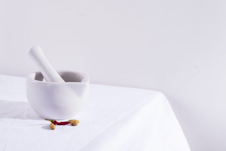 White porcelain mortar and pestle with chili peppers and cardamom isolated on textile table, copy...