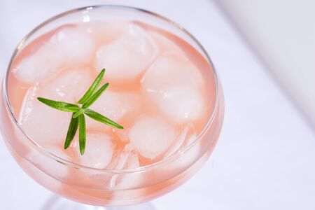 Pink cocktail with rosemary and ice on a white tablecloth on the tableの写真素材