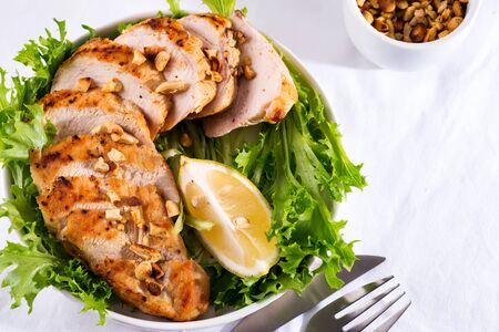 Grilled chicken breast with fresh frize salad, peanuts and lemon on a plate on stone backgroundの写真素材