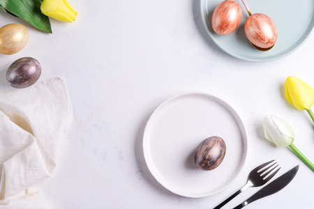 Easter table setting with spring tulips. Elegant empty plate, cutlery, napkin and golden eggs on...