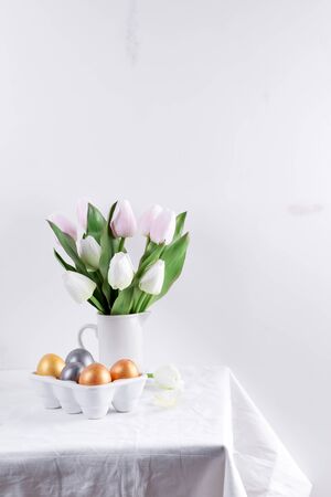 Golden Easter Eggs in ceramic egg tray with tulip on white table. Easter background or easter concept.の写真素材