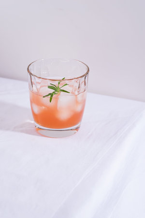 Pink cocktail with rosemary and ice in glass on a white tablecloth on the table