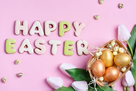 Congratulation Happy Easter card from handmade painted chicken and quail eggs, tulips flowers and text of homemade baked letters cookies on a pink background, copy space. Top view.の写真素材