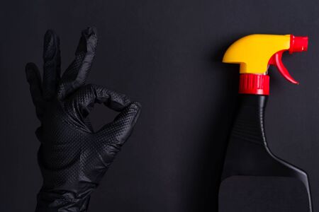OK sign made of woman's hand in a black rubber glove for cleaning and plastic spray bottle with yellow cap on the same color background, copy space.の写真素材