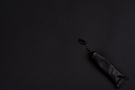 Black paint tin tube squeezed isolated on dark