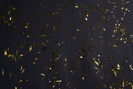 Golden bright confetti and coiled streamers, sparkles or glitter falling against black background. Merry Christmas festive black backdrop. Can be used for your creativity.の写真素材