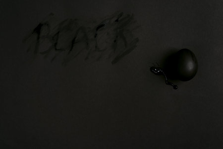 Handmade black painted egg on the same color background, copy space. Happy Easter card.