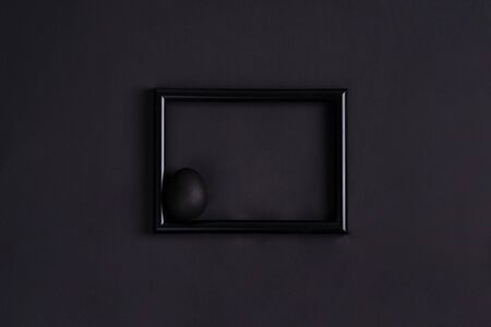 Easter photo frame with handmade painted black egg in black photo frame on a black background, copy space. Happy Easter concept.の写真素材