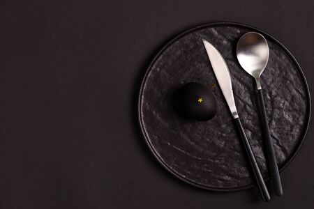 Tableware set from ceramic plate, spoon and knife with handmade painted black easter egg on the black background, copy space. Top view.の写真素材