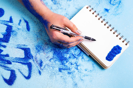 Empty white sheet of notebook with female's hand with pen above it, and decorative blue colored...