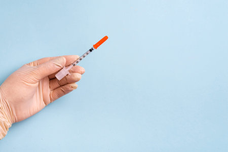 Womans hands in the medical gloves holds syringe on a light blue