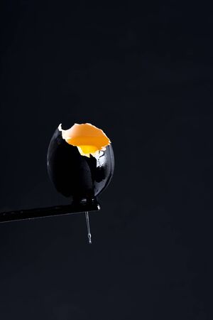 Handmade black painted and broken egg with fresh yellow yolk on the same color background, copy space.の写真素材