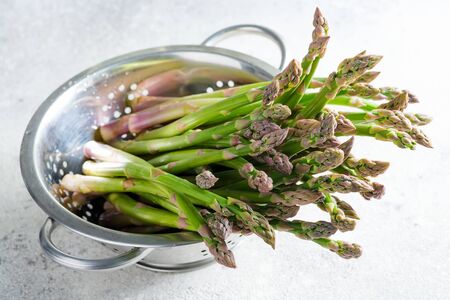 Raw organic asparagus in a colander ready for cooking healthy vegan food on a light grey marbleの写真素材